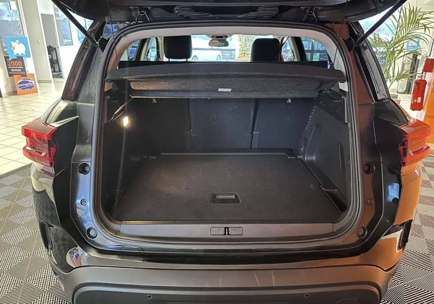 Coffre ouvert vu de l’arrière d’un Citroën C5 Aircross hybride noir 2025, intérieur spacieux avec cache-bagages relevé.