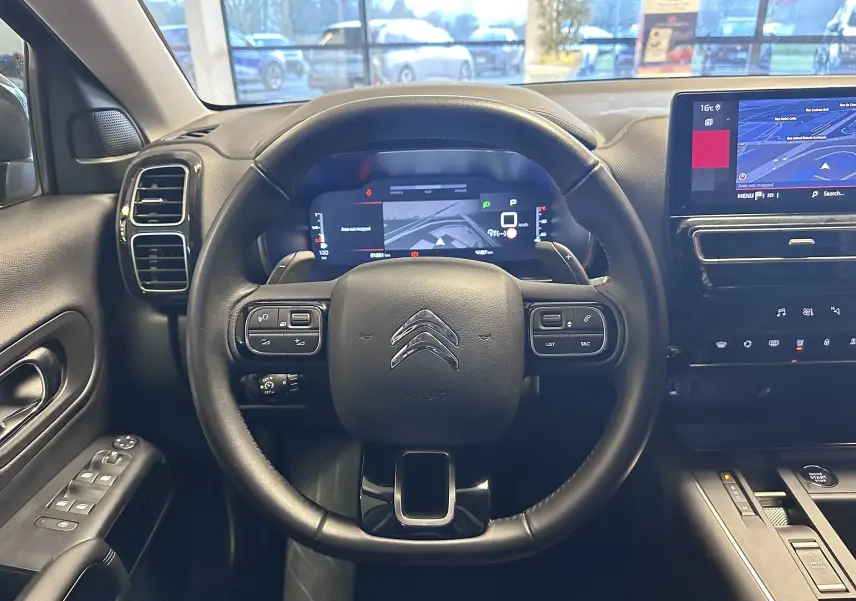 Vue intérieure centrée sur le volant noir de la Citroën C5 Aircross hybride 2025 avec tableau de bord numérique et écran tactile GPS.