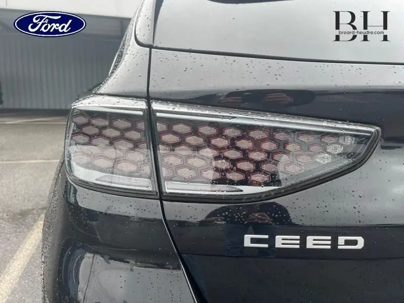 Gros plan sur le feu arrière droit d'une KIA CEE'D noir Basalte métallisé avec logo et pluie visible.
