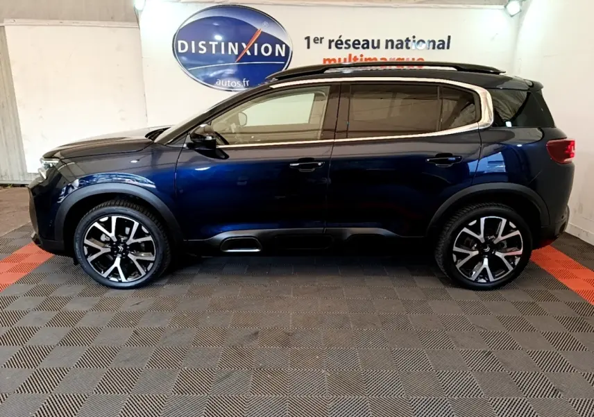 Vue de profil côté gauche d'un Citroën C5 Aircross 2023 bleu foncé avec jantes alliage et barres de toit noires.