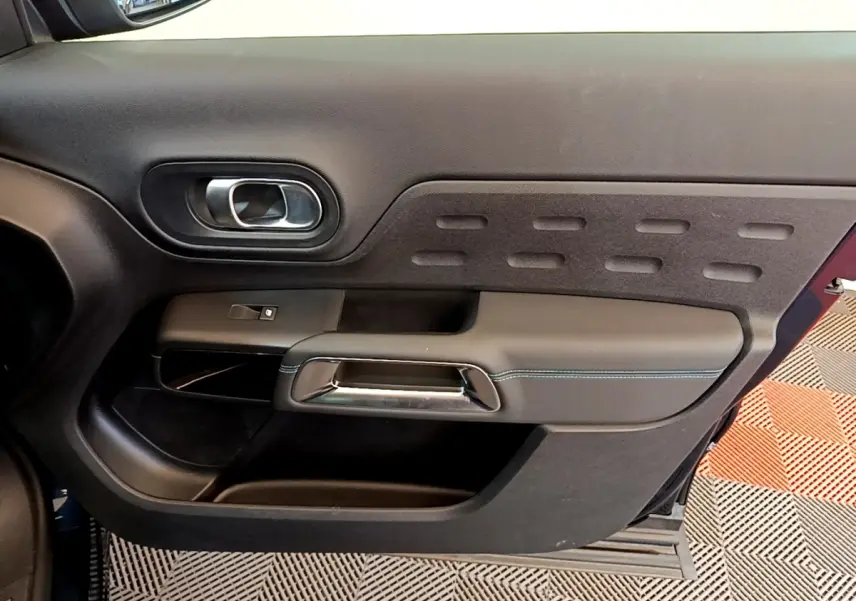 Vue intérieure côté gauche de la porte avant d’un Citroën C5 Aircross 2023 avec garniture noire et poignée chromée.