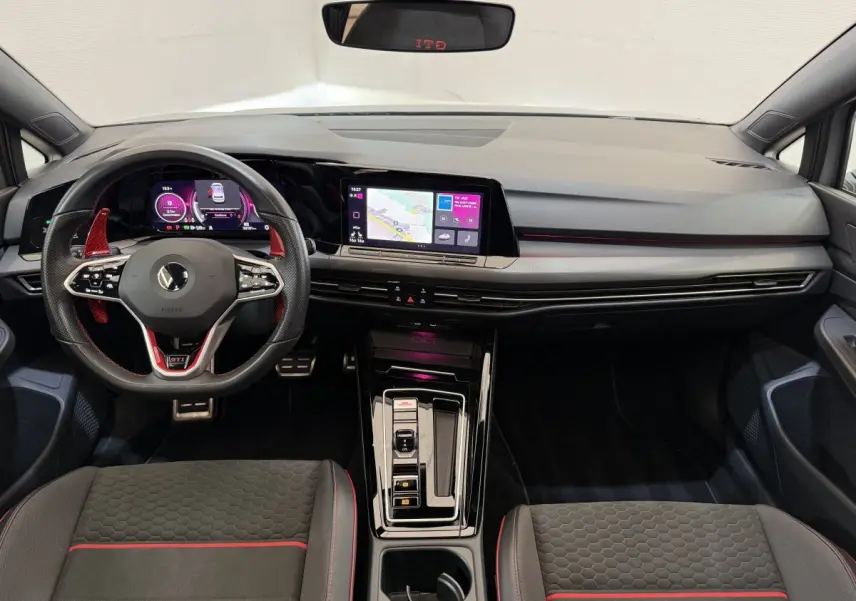 Vue intérieure frontale du tableau de bord de la Volkswagen Golf GTI Clubsport 2022 gris foncé avec éclairage d’ambiance rouge et écran tactile central.
