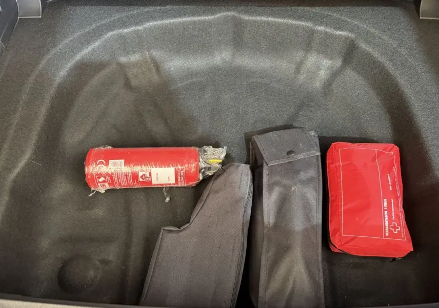 Coffre ouvert d’une Volkswagen Golf gris foncé, vue plongeante sur extincteur, trousse de secours et housses noires.