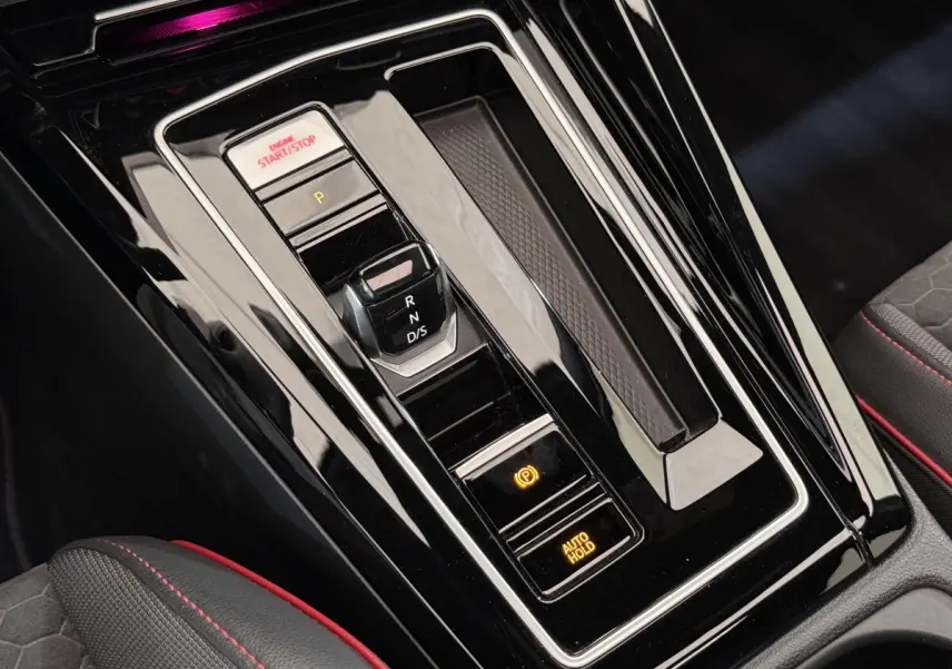 Gros plan sur la console centrale noire brillante avec levier de vitesses et boutons start/stop d’une Volkswagen Golf gris foncé.