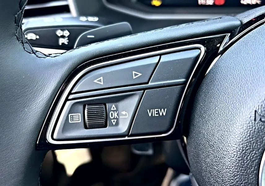 Gros plan sur les commandes gauche du volant cuir noir de l'Audi A1 Sportback 2026 avec boutons multifonctions.