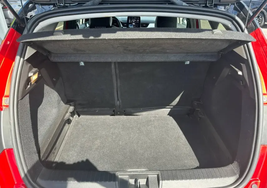 Coffre ouvert vu de l’arrière d’un Renault Captur 2024 rouge Flamme nacré, espace de chargement vide et tapis noir.