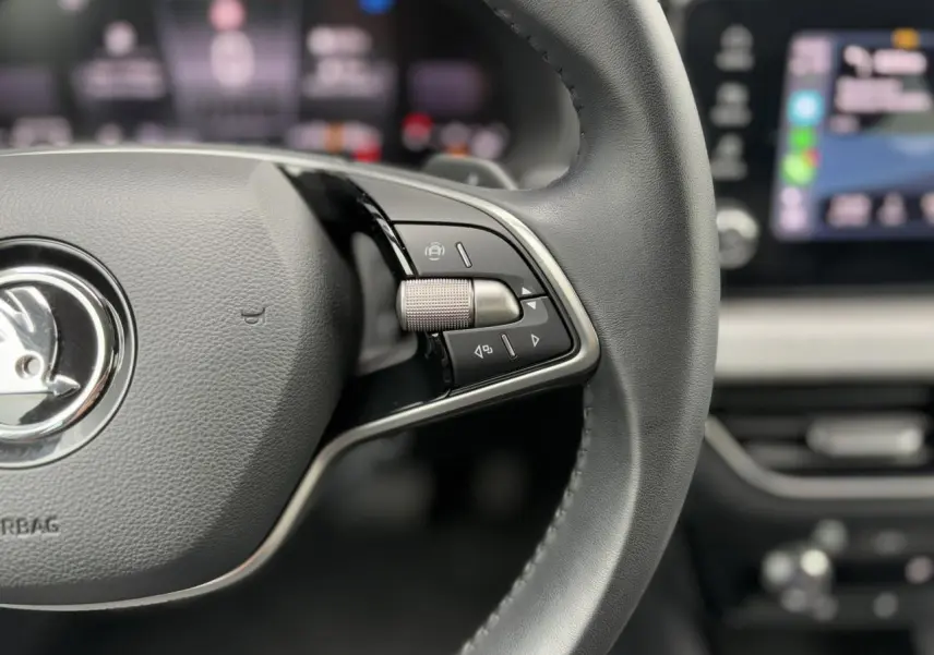 Gros plan sur le volant cuir multifonctions de la Skoda Scala 2024 avec commandes intégrées et tableau de bord flou en arrière-plan.