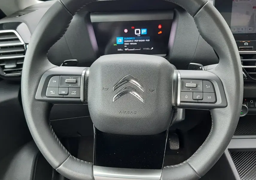 Vue rapprochée du volant noir de la Citroën C4 Hybrid 136 e-DSC6 Plus 2024 avec commandes intégrées et tableau de bord digital.