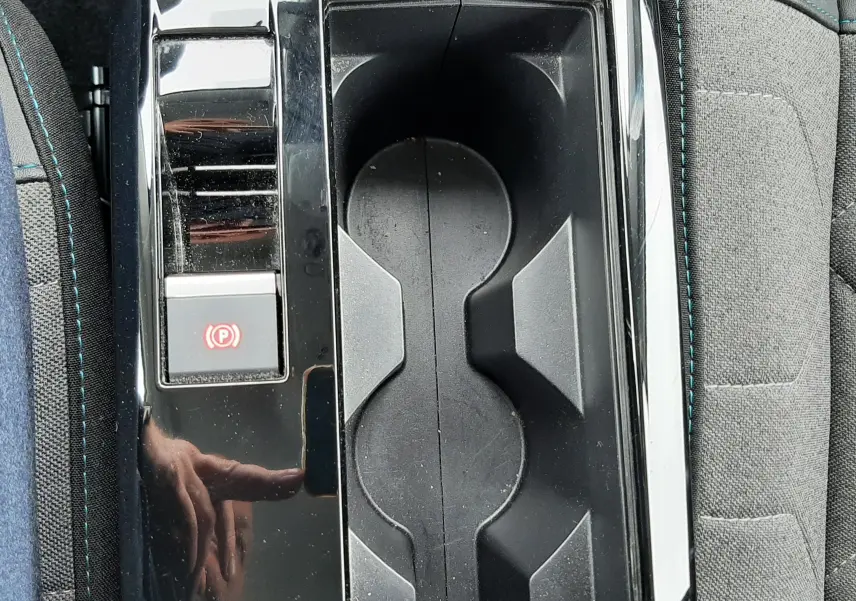 Gros plan sur la console centrale noire brillante avec porte-gobelets et bouton frein à main électrique de la Citroën C4 hybride.