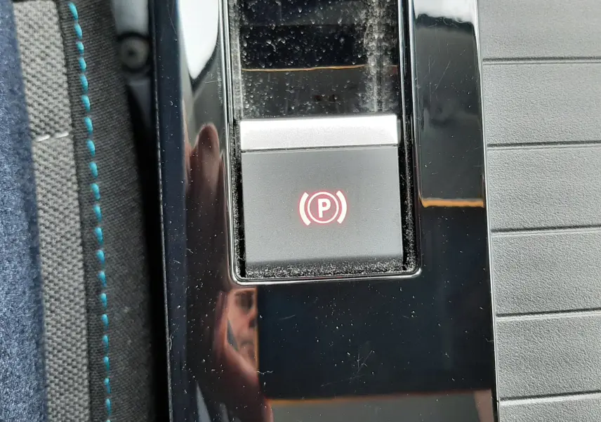 Gros plan sur le bouton de frein à main électronique rouge dans la console centrale noire d'une Citroën C4 Hybrid 2024.
