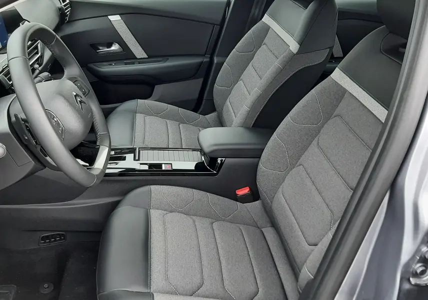 Vue intérieure côté conducteur du Citroën C4 Hybrid 136 gris acier, sièges tissu et cuir avec console centrale noire brillante.