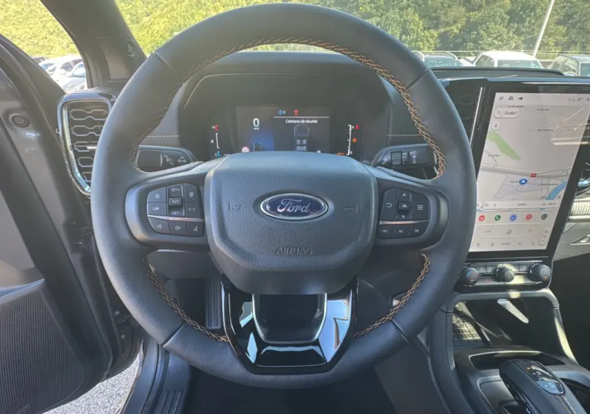Vue de face du volant en cuir noir avec surpiqûres marron du Ford Ranger 2025 gris carbone, tableau de bord numérique et écran tactile visible.