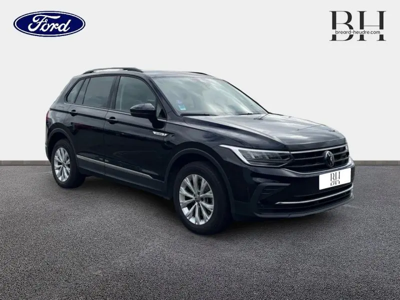 Volkswagen Tiguan 1.4 eHybrid noir nacré en 3/4 avant droit, avec jantes alu et barres de toit visibles.