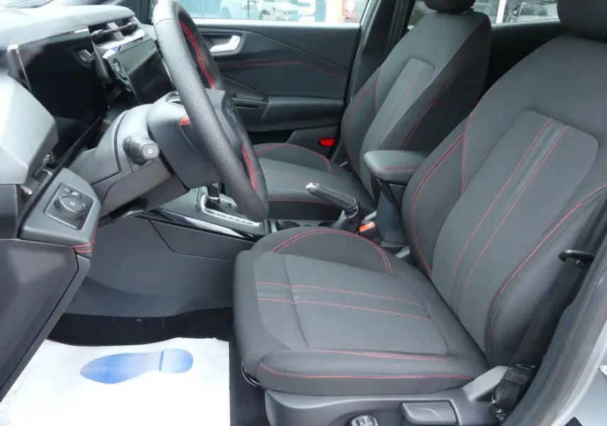 Vue intérieure côté conducteur du Ford Puma 2025, sièges tissu noirs avec surpiqûres rouges et volant sport.