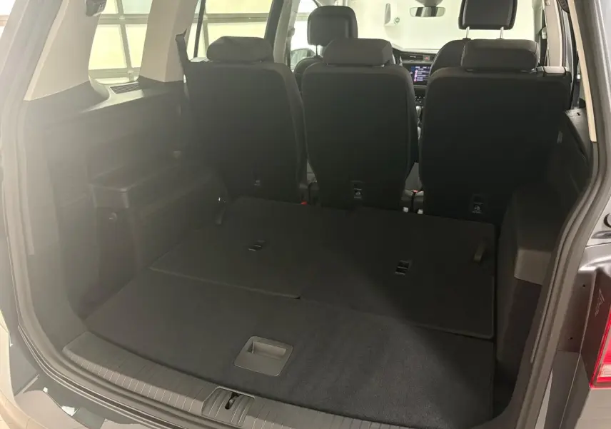 Vue arrière du coffre du Volkswagen Touran gris dauphin 2025 avec sièges rabattus et intérieur noir.