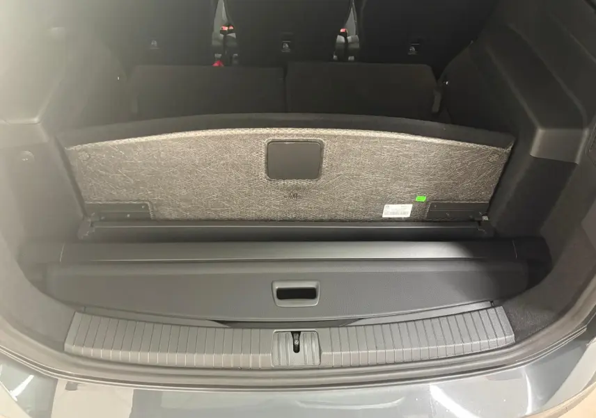 Vue du coffre arrière ouvert du Volkswagen Touran 2025 gris dauphin, avec cache-bagages et sièges rabattus visibles.