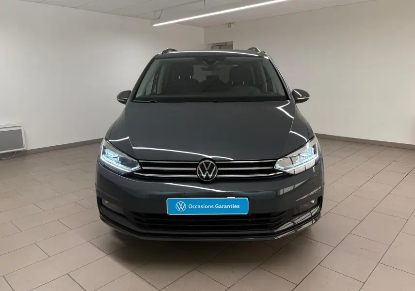Volkswagen Touran gris dauphin vu de face en intérieur, avec phares LED allumés et calandre chromée.