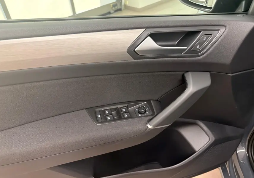 Vue rapprochée de la porte avant gauche du Volkswagen Touran gris dauphin, avec commandes des vitres et poignée intégrée.