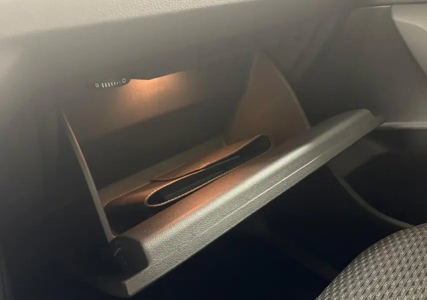Vue intérieure du Volkswagen Touran 2025 montrant la boîte à gants ouverte avec un éclairage doux et un livret à l'intérieur.