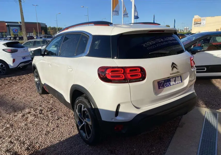 Vue 3/4 arrière droite d'un Citroën C5 Aircross blanc nacré avec barres de toit Deep Red anodisé et jantes bi-ton.