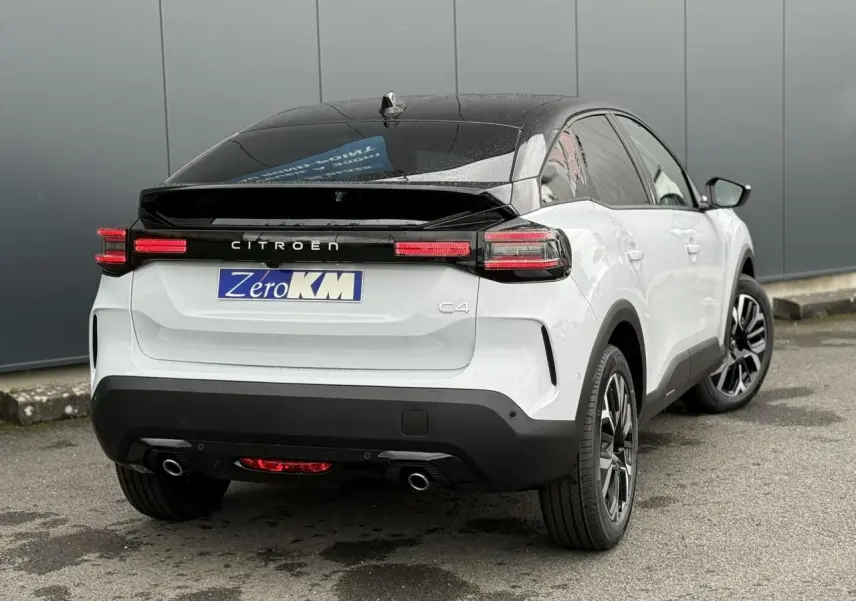 Vue 3/4 arrière droite d'une Citroën C4 blanche Okénite avec toit noir et feux arrière LED allumés.