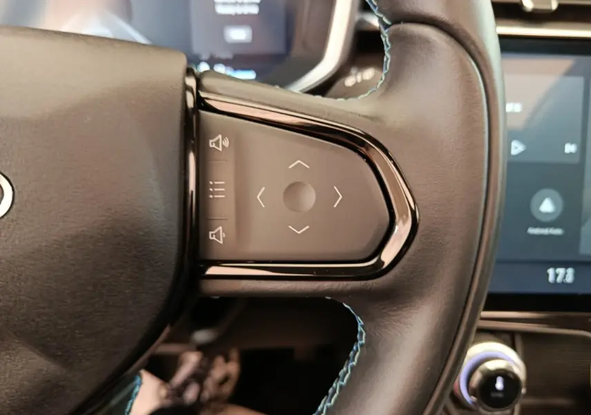 Gros plan sur les commandes tactiles du volant en cuir noir du Link & Co 01 hybride rechargeable, avec écran tactile en arrière-plan.