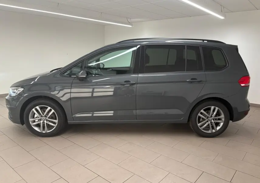 Profil côté gauche d'un Volkswagen Touran 2025 gris dauphin avec jantes alliage 17 pouces en intérieur lumineux.