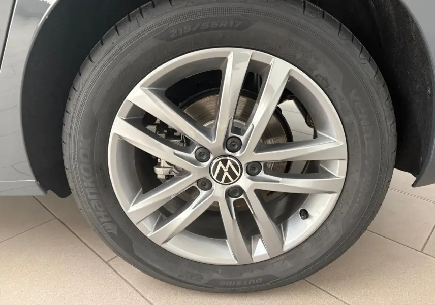 Gros plan sur la roue avant droite du Volkswagen Touran gris dauphin avec jante alliage 17 pouces et logo VW central.