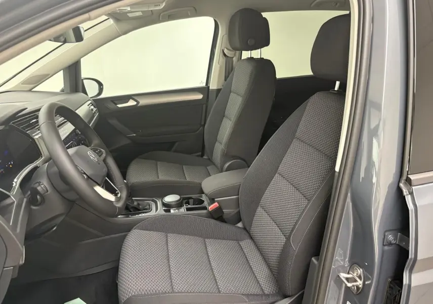 Vue intérieure côté conducteur du Volkswagen Touran gris Dauphin 2025, mettant en valeur les sièges tissu et le tableau de bord moderne.