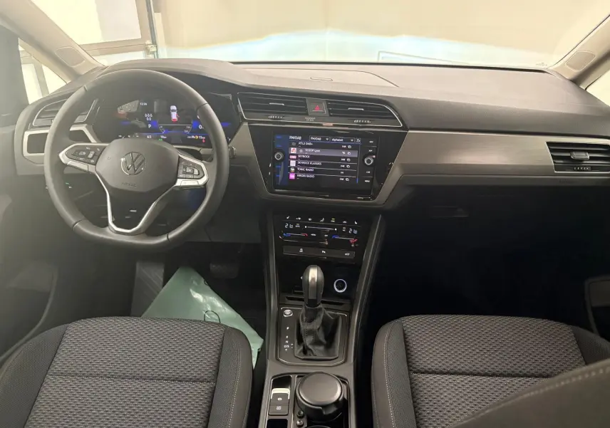 Vue intérieure frontale du tableau de bord et volant du Volkswagen Touran gris dauphin avec écran tactile et console centrale moderne.