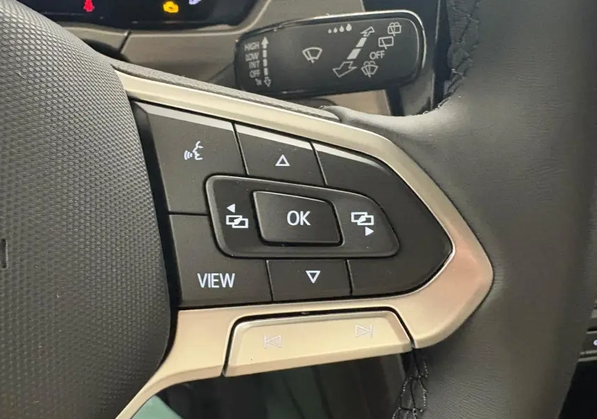 Gros plan sur les commandes multifonctions noires et argent du volant cuir du Volkswagen Touran gris dauphin 2025.