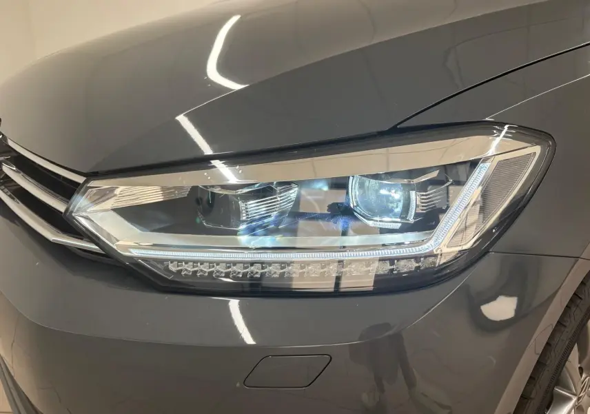 Gros plan sur le phare avant droit du Volkswagen Touran gris dauphin 2025 avec éclairage LED distinctif.