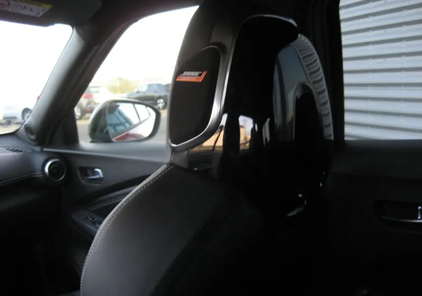 Gros plan sur l'appui-tête avant gauche noir brillant avec logo Bose, intérieur cuir du Nissan Juke 1.6 Hybrid 2024.