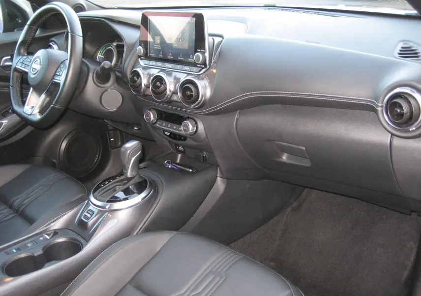 Vue intérieure côté conducteur du tableau de bord et console centrale du Nissan Juke 1.6 Hybrid 143 Tekna avec sellerie cuir noire.