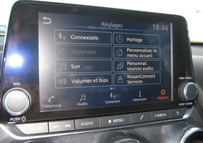 Écran tactile central du Nissan Juke 2024 en gros plan, affichant le menu des réglages audio et connexions.