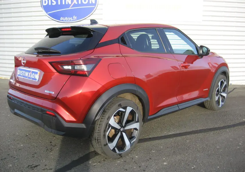 Vue 3/4 arrière droite d'un Nissan Juke 1.6 Hybrid rouge 2024 avec jantes bi-ton et toit noir.