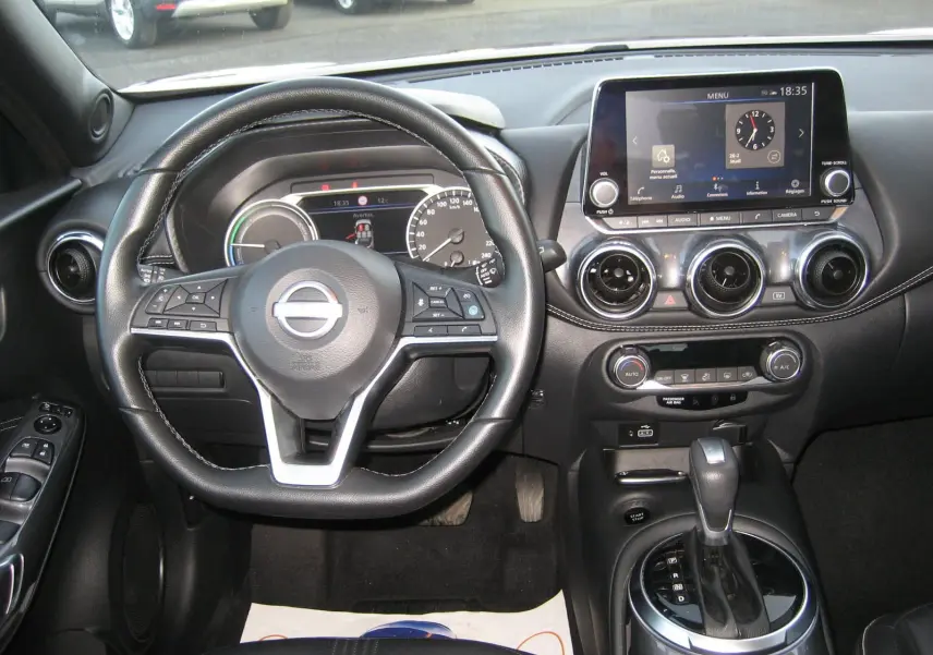 Vue intérieure centrée sur le volant et la console centrale du Nissan Juke 1.6 Hybrid rouge avec écran tactile et boîte auto.