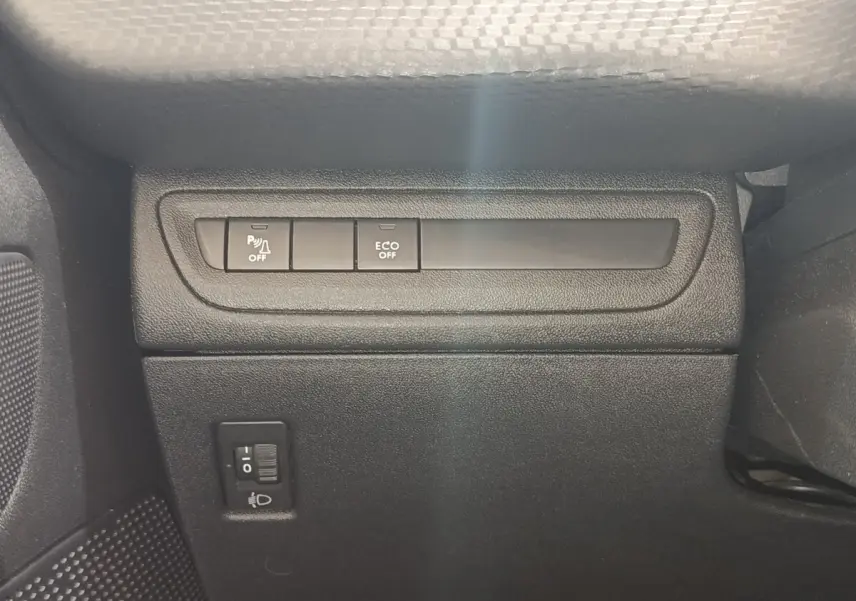Gros plan sur les commandes de désactivation du parking assisté et mode ECO, côté gauche intérieur d’un Peugeot 2008 gris foncé.