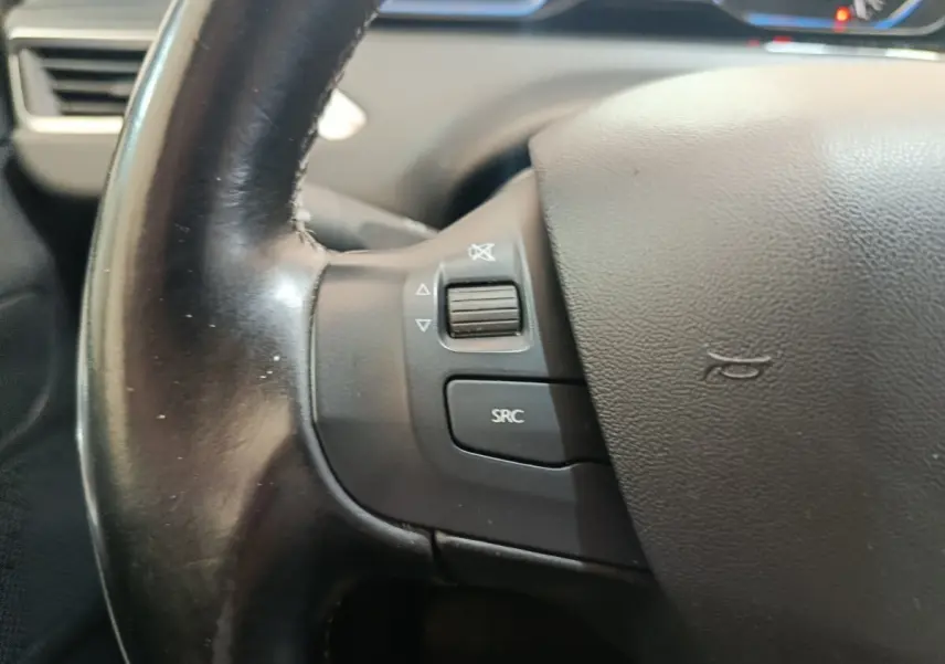 Gros plan sur le volant en cuir noir côté gauche du Peugeot 2008 gris foncé, avec commandes audio intégrées.