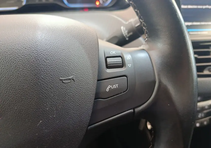 Gros plan sur le volant cuir noir côté droit du Peugeot 2008 gris foncé, avec commandes intégrées et tableau de bord en arrière-plan.
