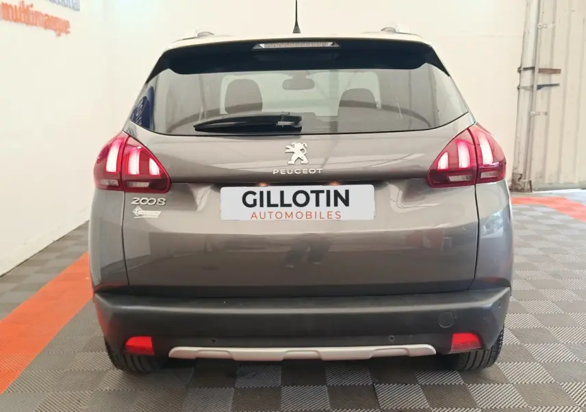 Vue arrière d'un Peugeot 2008 gris foncé avec feux allumés et logo visible dans un showroom.