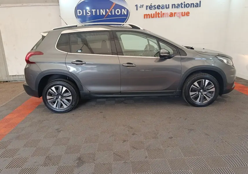 Peugeot 2008 gris foncé vue de profil côté gauche, avec jantes alliage et barres de toit chromées.