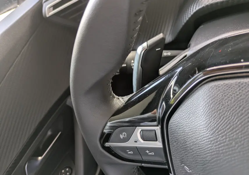 Gros plan sur les commandes au volant côté gauche du Peugeot 2008 Hybrid 145, avec finition noire brillante.