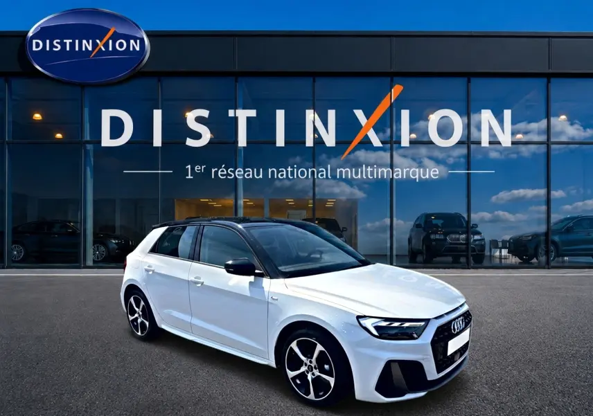 Audi A1 Sportback blanc et noir en vue 3/4 avant droit, avec jantes alu et toit noir brillant devant un showroom Distinxion.