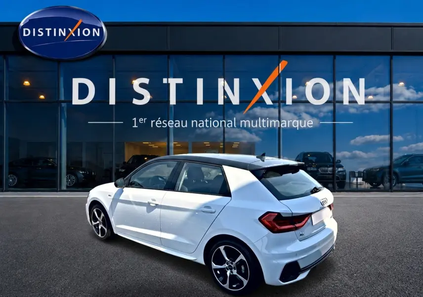 Audi A1 Sportback blanc toit noir en 3/4 arrière droit, avec jantes alu et becquet arrière visible devant showroom Distinxion.