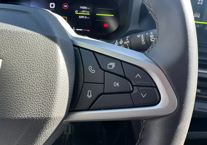 Gros plan sur le volant multifonction noir du Dacia Duster 2025, avec commandes vocales et téléphone côté droit.