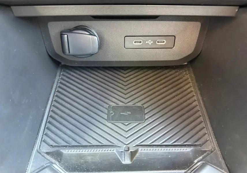 Gros plan sur la zone de recharge avec ports USB-C et prise 12V dans le compartiment central noir du Dacia Duster.