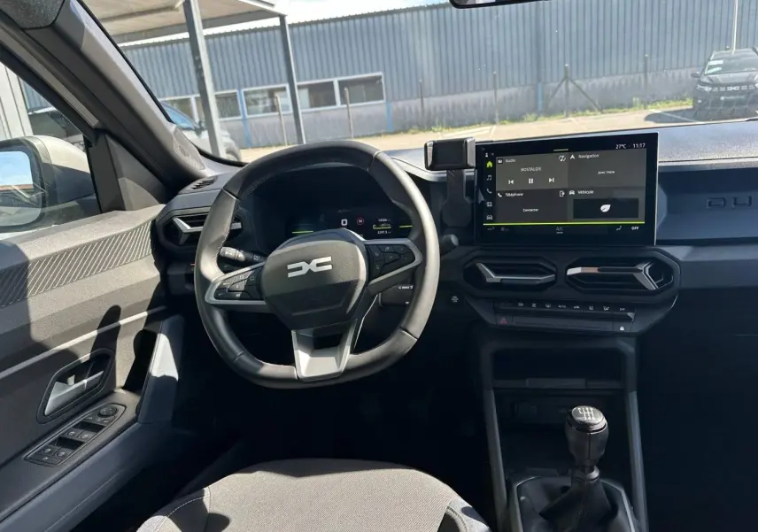 Vue intérieure côté conducteur du Dacia Duster 2025, montrant le volant multifonction, écran tactile et levier de vitesses manuel.