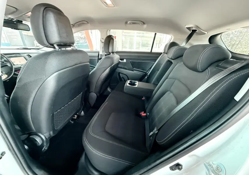 Intérieur arrière du Kia Sportage 2015 blanc, sièges noirs avec accoudoir central et porte-gobelets visibles.