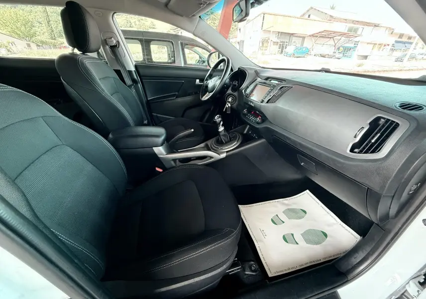 Intérieur côté passager du Kia Sportage blanc de 2015, montrant sièges noirs et tableau de bord avec console centrale.